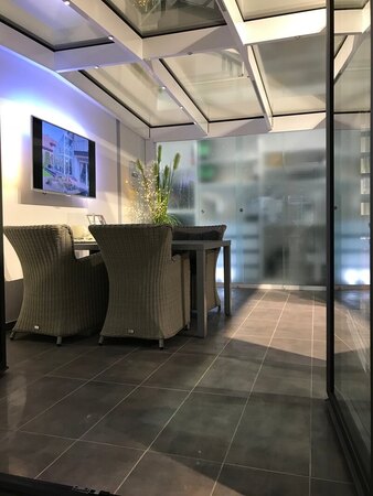 Moderner Wintergarten mit Glasdach, gemütlicher Sitzecke und stilvoller LED-Beleuchtung.